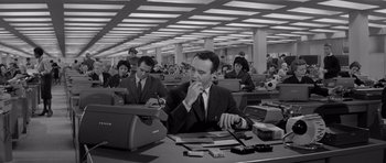 Movie still from “The Apartment” (1960), directed by Billy Wilder – A man sitting at a desk in front of other people; Wide shot, High angle