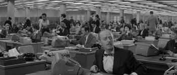 Movie still from “The Apartment” (1960), directed by Billy Wilder – A man sitting at a desk in front of many other people; Medium shot, High angle