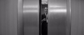 Movie still from “The Apartment” (1960), directed by Billy Wilder – A black and white photo of a man in a suit and tie; Medium shot, Low angle