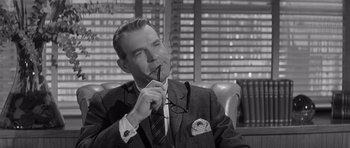 Movie still from “The Apartment” (1960), directed by Billy Wilder – An older man wearing a suit and tie holding a pair of glasses; Close Up shot, Over the shoulder angle