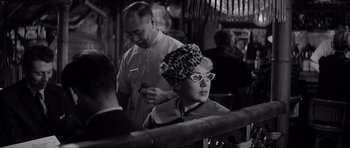 Movie still from “The Apartment” (1960), directed by Billy Wilder – A woman with a head scarf and glasses sitting at a table with a man; Close Up shot, Over the shoulder angle