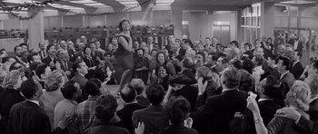 Movie still from “The Apartment” (1960), directed by Billy Wilder – An old black and white photo of a crowd of people sitting and standing; Wide shot, High angle