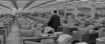 Movie still from “The Apartment” (1960), directed by Billy Wilder – A black and white photo of a man standing in a room full of boxes; Wide shot, High angle