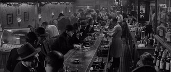 Movie still from “The Apartment” (1960), directed by Billy Wilder – A group of men sitting at a bar drinking and smoking cigarettes; Wide shot, High angle