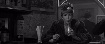 Movie still from “The Apartment” (1960), directed by Billy Wilder – A woman sitting at a table drinking a drink; Close Up shot, High angle