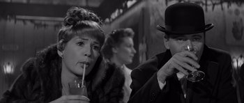 Movie still from “The Apartment” (1960), directed by Billy Wilder – A woman drinking a drink in front of a man in a top hat; Close Up shot, Over the shoulder angle