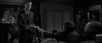 Movie still from “The Apartment” (1960), directed by Billy Wilder – A man handing a tray to another man in a room; Medium shot, Over the shoulder angle