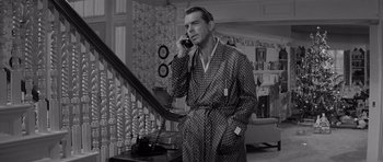 Movie still from “The Apartment” (1960), directed by Billy Wilder – A man talking on a phone while standing in front of a staircase; Medium shot, High angle