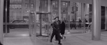 Movie still from “The Apartment” (1960), directed by Billy Wilder – A man walking down the sidewalk in front of a building; Wide shot, Over the shoulder angle