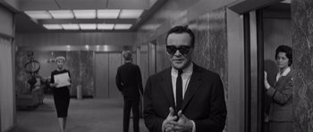 Movie still from “The Apartment” (1960), directed by Billy Wilder – A black and white photo of a man in a suit and sunglasses; Medium shot, Low angle