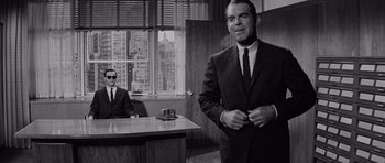 Movie still from “The Apartment” (1960), directed by Billy Wilder – A man in a suit standing in front of a desk in an office; Medium shot, Over the shoulder angle