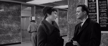 Movie still from “The Apartment” (1960), directed by Billy Wilder – A woman wearing a coat and hat talking to a man in a suit; Medium shot, Over the shoulder angle