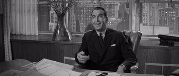 Movie still from “The Apartment” (1960), directed by Billy Wilder – A man sitting at a desk in a suit and tie; Medium shot, Over the shoulder angle