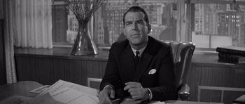 Movie still from “The Apartment” (1960), directed by Billy Wilder – A man in a suit sitting at a table in front of a window; Medium shot, Over the shoulder angle