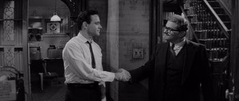 Movie still from “The Apartment” (1960), directed by Billy Wilder – Two men shaking hands in a black and white photo; Medium shot, Over the shoulder angle