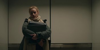 Movie still from “The Assistant” (2019), directed by Kitty Green – A woman holding a stack of papers in her arms; Medium shot, Low angle
