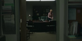 Movie still from “The Assistant” (2019), directed by Kitty Green – A person sitting at a desk in a room; Wide shot, Over the shoulder angle
