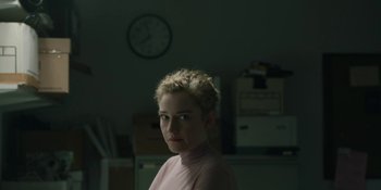 Movie still from “The Assistant” (2019), directed by Kitty Green – A woman with blonde hair is standing in front of a wall clock; Medium shot, Over the shoulder angle