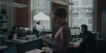 Movie still from “The Assistant” (2019), directed by Kitty Green – A woman standing in an office holding papers; Medium shot, Over the shoulder angle
