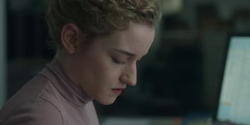 Movie still from “The Assistant” (2019), directed by Kitty Green – A young woman with blonde curly hair is looking down; Close Up shot, Over the shoulder angle