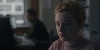 Movie still from “The Assistant” (2019), directed by Kitty Green – A woman sitting in front of a man in a room; Close Up shot, Over the shoulder angle
