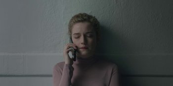 Movie still from “The Assistant” (2019), directed by Kitty Green – A young woman talking on a cell phone while leaning against a wall; Close Up shot, High angle
