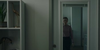Movie still from “The Assistant” (2019), directed by Kitty Green – A woman standing in front of a mirror in a room; Medium shot, Over the shoulder angle