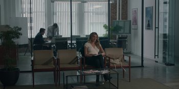 Movie still from “The Assistant” (2019), directed by Kitty Green – A woman sitting on a chair in a waiting room; Wide shot, High angle
