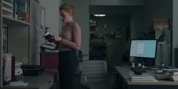 Movie still from “The Assistant” (2019), directed by Kitty Green – A woman standing in front of a stack of books; Medium shot, Low angle
