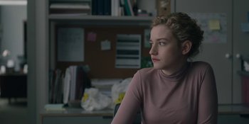 Movie still from “The Assistant” (2019), directed by Kitty Green – A woman sitting at a desk in front of a wall; Close Up shot, Over the shoulder angle