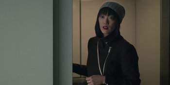 Movie still from “The Assistant” (2019), directed by Kitty Green – A young woman in a black jacket and a gray hat; Close Up shot, Over the shoulder angle