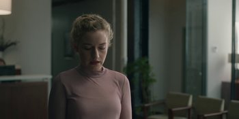 Movie still from “The Assistant” (2019), directed by Kitty Green – A woman in a pink shirt is looking down; Medium shot, Over the shoulder angle
