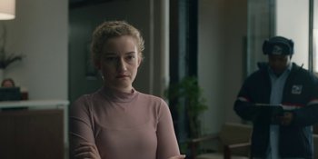Movie still from “The Assistant” (2019), directed by Kitty Green – A woman in a pink shirt is standing in a room; Medium shot, Over the shoulder angle
