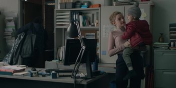 Movie still from “The Assistant” (2019), directed by Kitty Green – A woman holding a child in her arms; Medium shot, Over the shoulder angle