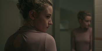 Movie still from “The Assistant” (2019), directed by Kitty Green – A young woman looking at her reflection in a mirror; Close Up shot, Over the shoulder angle