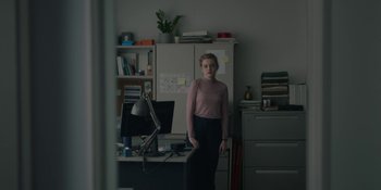 Movie still from “The Assistant” (2019), directed by Kitty Green – A woman standing in front of a computer desk; Medium shot, Over the shoulder angle