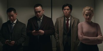 Movie still from “The Assistant” (2019), directed by Kitty Green – Two men in suits and ties standing next to each other looking at a cell phone; Medium shot, Low angle