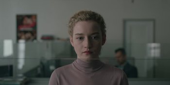 Movie still from “The Assistant” (2019), directed by Kitty Green – A woman with blonde curly hair wearing a purple shirt; Close Up shot, Over the shoulder angle