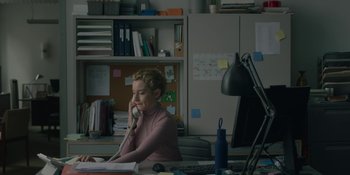 Movie still from “The Assistant” (2019), directed by Kitty Green – A woman sitting at a desk talking on the phone; Medium shot, Over the shoulder angle