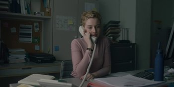 Movie still from “The Assistant” (2019), directed by Kitty Green – A woman sitting at a desk talking on a phone; Medium shot, High angle