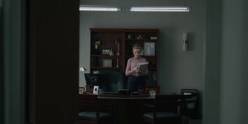 Movie still from “The Assistant” (2019), directed by Kitty Green – A person sitting at a desk in a room; Medium shot, Over the shoulder angle