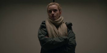 Movie still from “The Assistant” (2019), directed by Kitty Green – A woman wearing a jacket and a scarf is posing for a picture; Close Up shot, Low angle