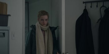 Movie still from “The Assistant” (2019), directed by Kitty Green – A young woman wearing a coat and a scarf in front of a bathroom mirror; Medium shot, Over the shoulder angle