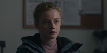 Movie still from “The Assistant” (2019), directed by Kitty Green – A woman with blonde curly hair wearing a pink shirt; Close Up shot, Over the shoulder angle