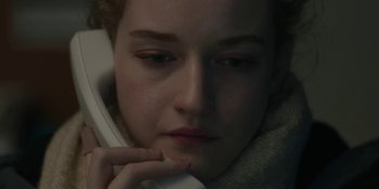 Movie still from “The Assistant” (2019), directed by Kitty Green – A young woman holding a phone up to her face; Close Up shot, High angle