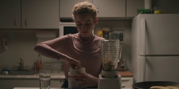Movie still from “The Assistant” (2019), directed by Kitty Green – A woman in a pink shirt is making a smoothie; Medium shot, Over the shoulder angle
