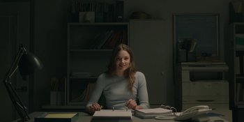 Movie still from “The Assistant” (2019), directed by Kitty Green – A woman sitting at a desk in front of papers; Medium shot, Over the shoulder angle