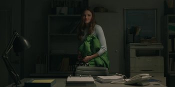 Movie still from “The Assistant” (2019), directed by Kitty Green – A woman standing in a room with a green bag; Medium shot, Over the shoulder angle