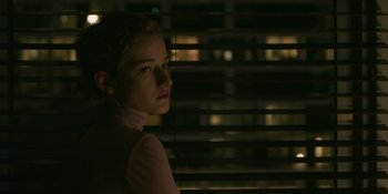 Movie still from “The Assistant” (2019), directed by Kitty Green – A young girl is standing in front of a window at night; Close Up shot, Over the shoulder angle
