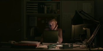Movie still from “The Assistant” (2019), directed by Kitty Green – A woman sitting at a desk using a laptop computer; Medium shot, High angle